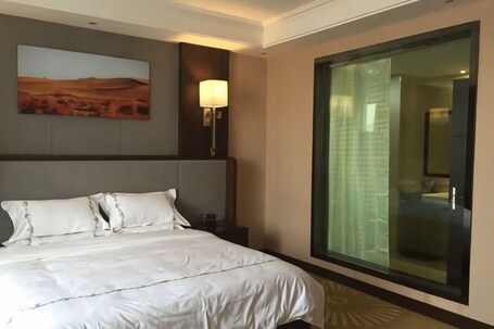 A hotel room with a large bed, a nightstand, a wall-mounted lamp, a painting, and a large window with a view.. KAIYUE HOTEL