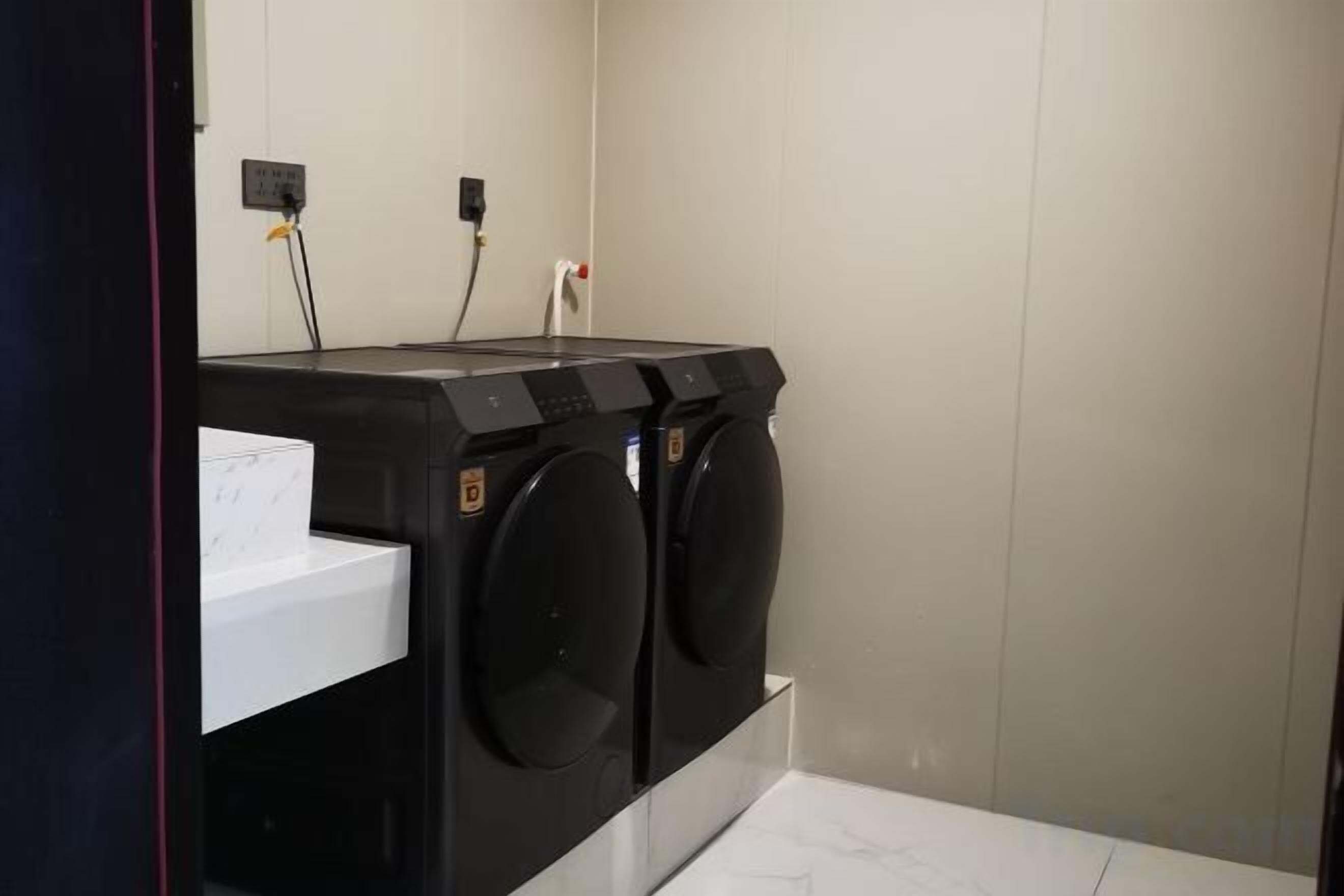 A laundry area with two stacked washing machines and a white sink.
