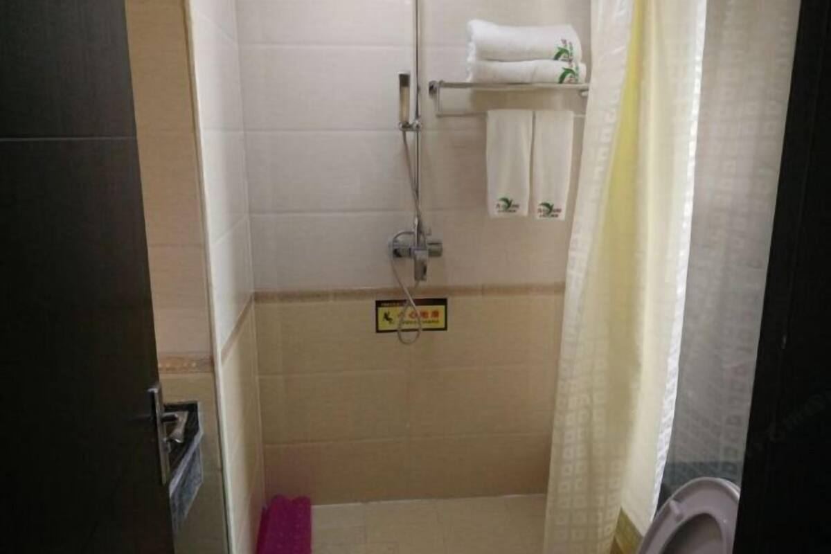 Un baño pequeño, con azulejos, que incluye una ducha, un inodoro y un perchero con toallas.