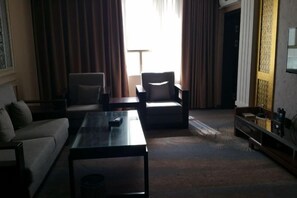 A hotel room with a sofa, two armchairs, a coffee table, a TV, and a window with curtains. - KAIYUE HOTEL (Qiemo)