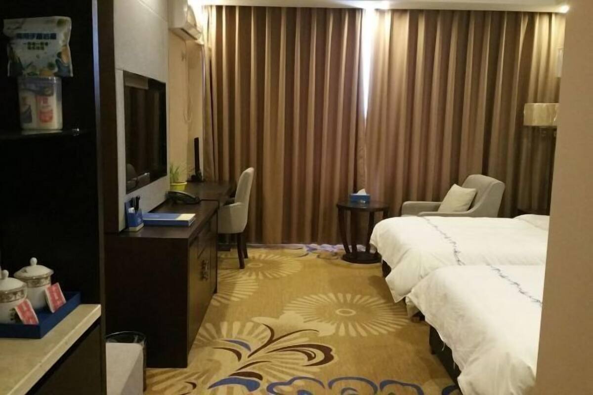 Habitación de hotel con cama, escritorio, silla, mesita y cortina.