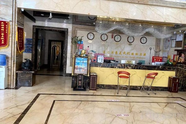 A hotel reception area with a marble floor, a reception desk, and a wall clock. - KAIYUE HOTEL (Qiemo)