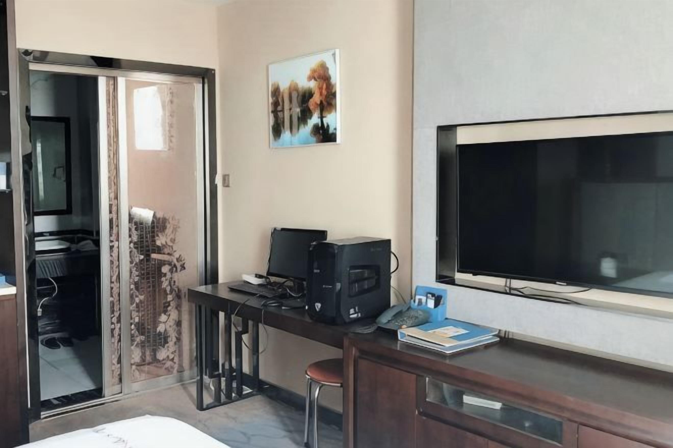 Habitación de hotel con escritorio, televisión, cama y puerta corrediza que da a un balcón.