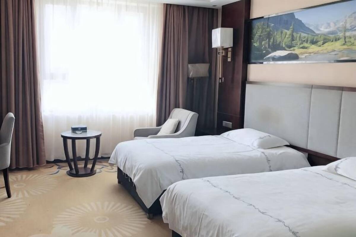 Una habitación de hotel con dos camas, una silla, una mesita y un cuadro en la pared.