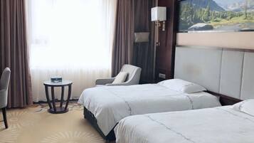 A hotel room with two beds, a chair, a small table, and a painting on the wall.