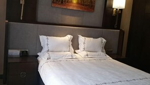 A hotel room with a large bed, a nightstand, a wall-mounted lamp, and a painting above the bed. - KAIYUE HOTEL (Qiemo)