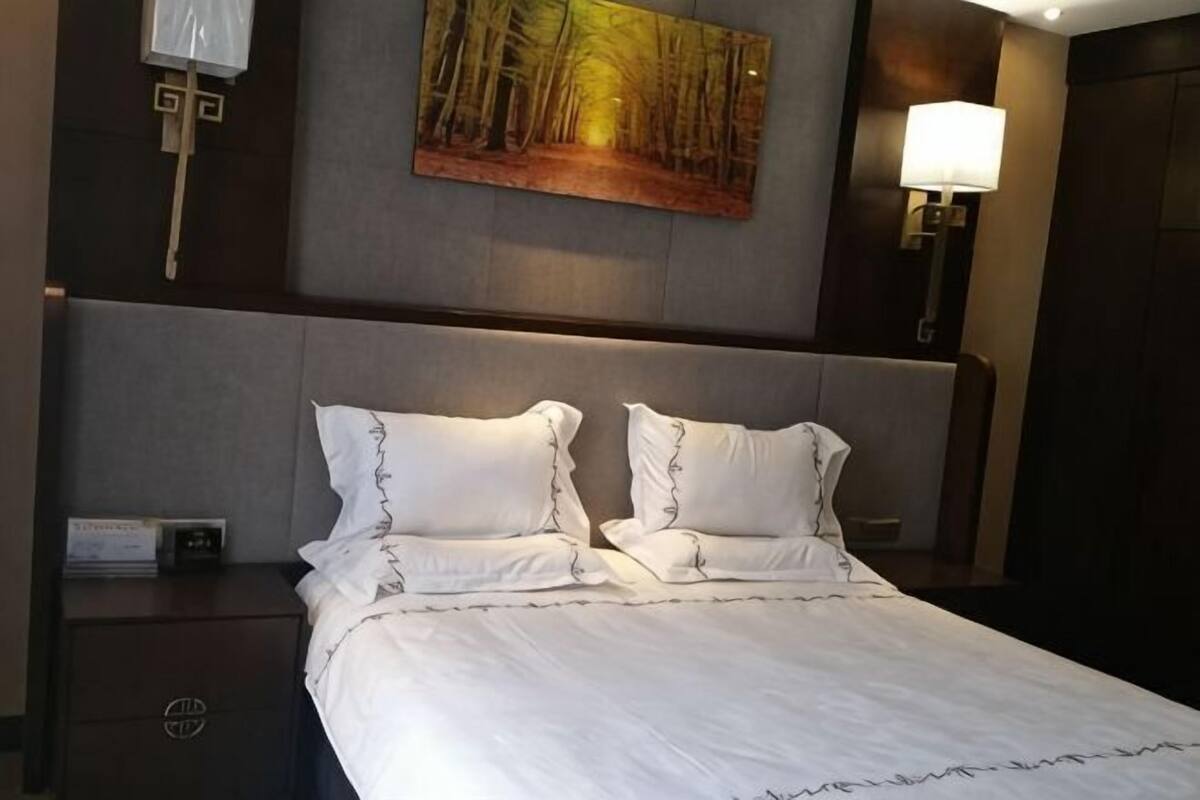 Habitación de hotel con una cama grande, una mesita de noche, una lámpara de pared y un cuadro sobre la cama.