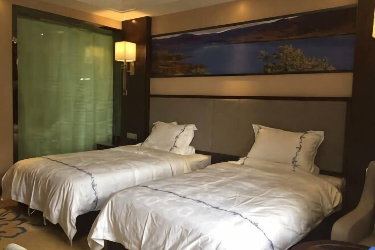 Una habitación de hotel con dos camas, un cuadro grande, una mesita de noche y una ventana con cortinas.