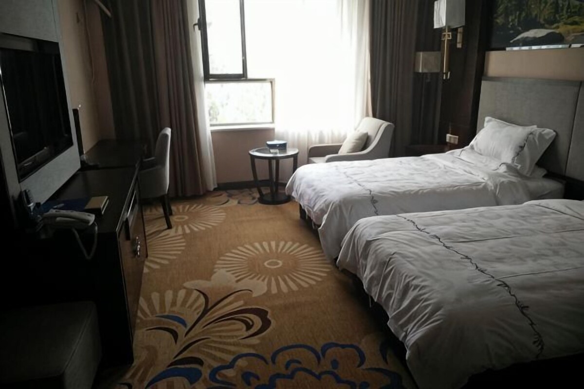 A hotel room with two beds, a desk, a chair, a television, and a window with curtains.