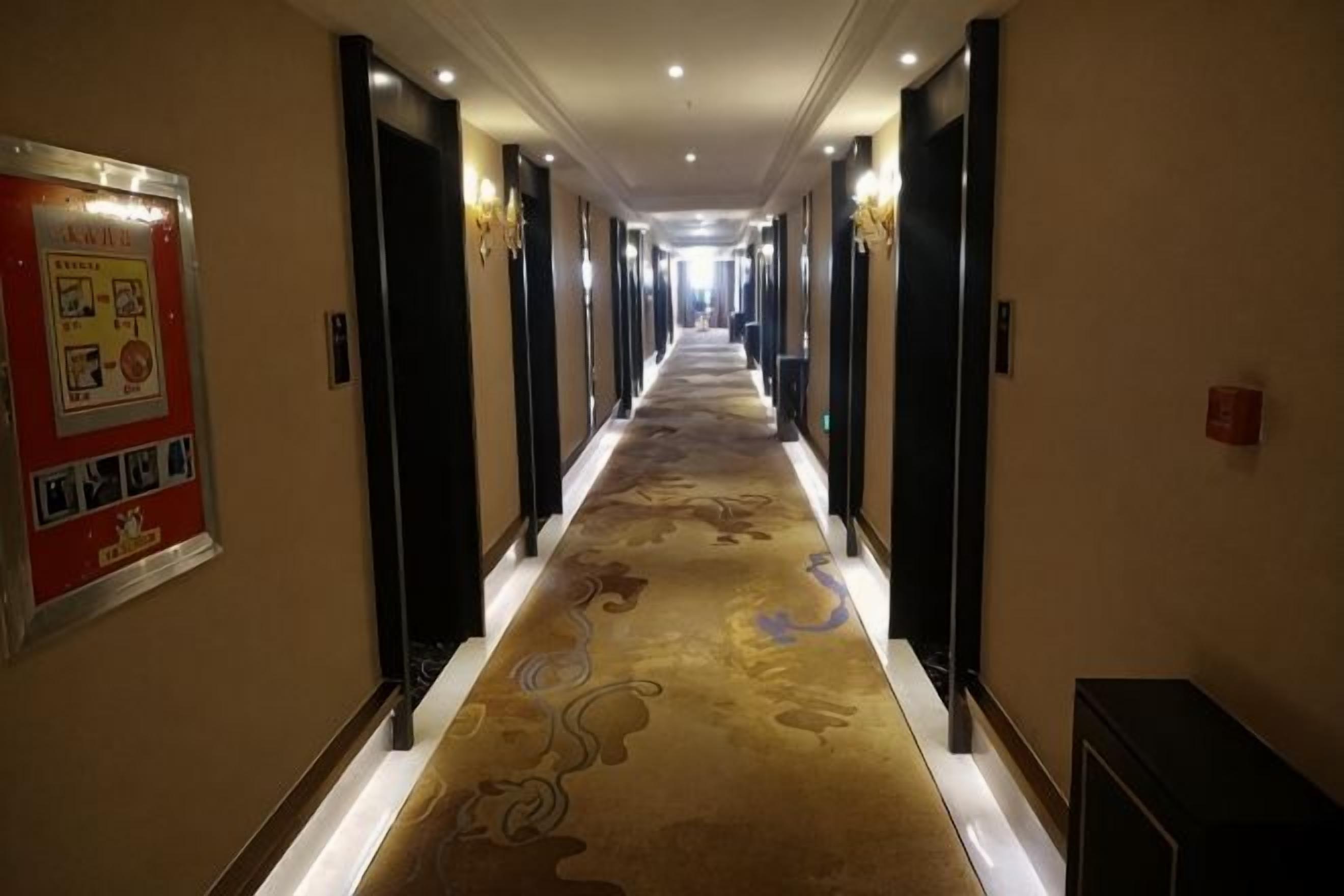 Un pasillo de hotel con piso alfombrado, puertas a ambos lados y un cartel en la pared izquierda.