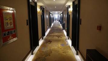Un pasillo de hotel con piso alfombrado, puertas a ambos lados y un cartel en la pared izquierda.