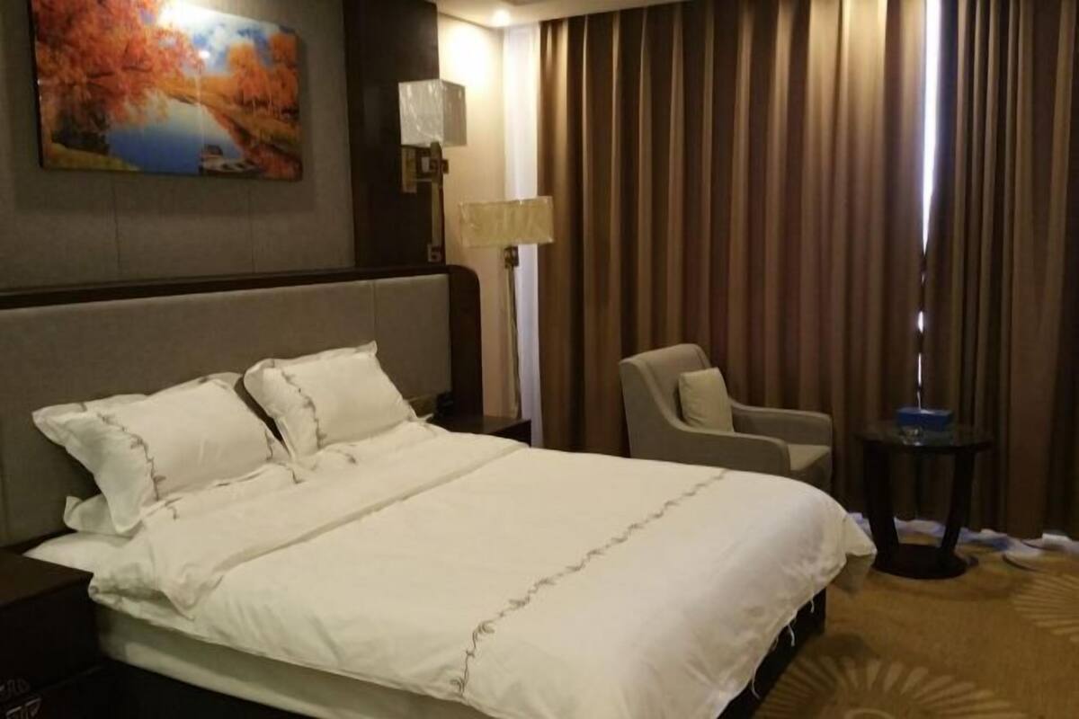 Una habitación de hotel con una cama grande, una silla, una lámpara y un cuadro en la pared.
