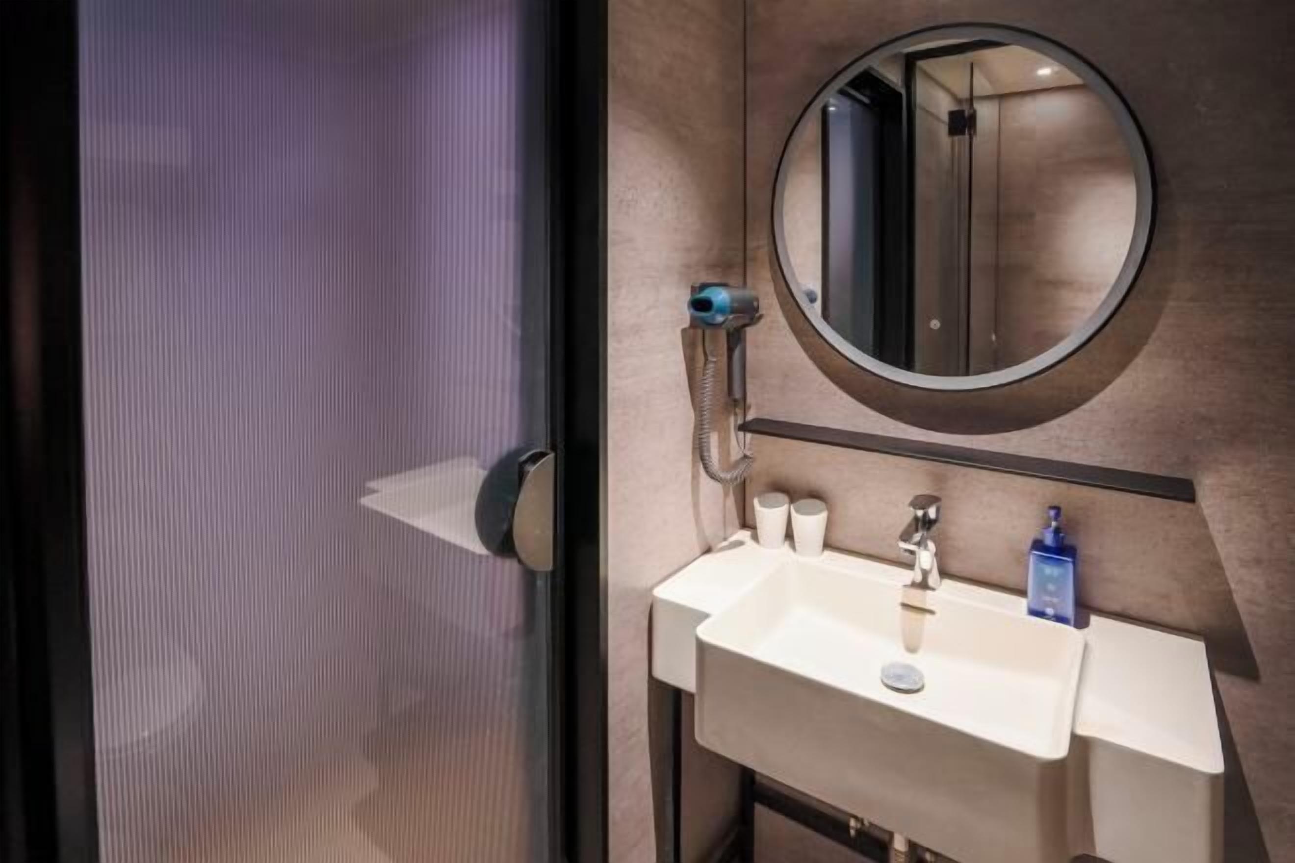 Une salle de bain avec un miroir rond, un lavabo et un porte-serviettes.