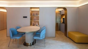 A modern dining area with a round table and four blue chairs, a yellow bench, and a built-in bookshelf with framed pictures. - HanTing Hotel (Tianjin Railway Station Italian Style Street) (Tianjin)