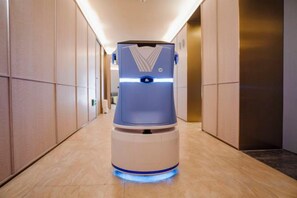 A corridor with a robotic vacuum cleaner in the center, a door on the right, and a wall with a textured pattern. - HanTing Hotel (Tianjin Railway Station Italian Style Street) (Tianjin)