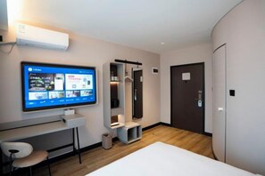A hotel room with a flat-screen TV mounted on the wall, a small desk with a chair, a wardrobe, and a door. - HanTing Hotel (Tianjin Railway Station Italian Style Street) (Tianjin)