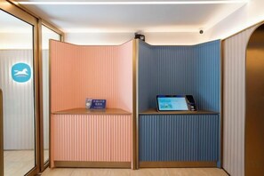 Zona de recepción con un mostrador, una computadora, pared azul y pared rosa.