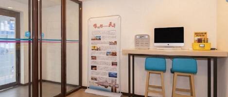 A reception area with a glass door entrance, a computer monitor, a small table, and two blue bar stools.