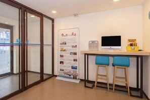 Un área de recepción con puerta de entrada de vidrio, un monitor de computadora, una mesita pequeña y dos taburetes azules.