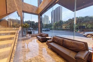 A modern interior with a marble floor, leather sofa, and large windows offering a view of the street and buildings. - Fugang Hotel(Xuchang College High Speed Rail East Station Store) (Xuchang)