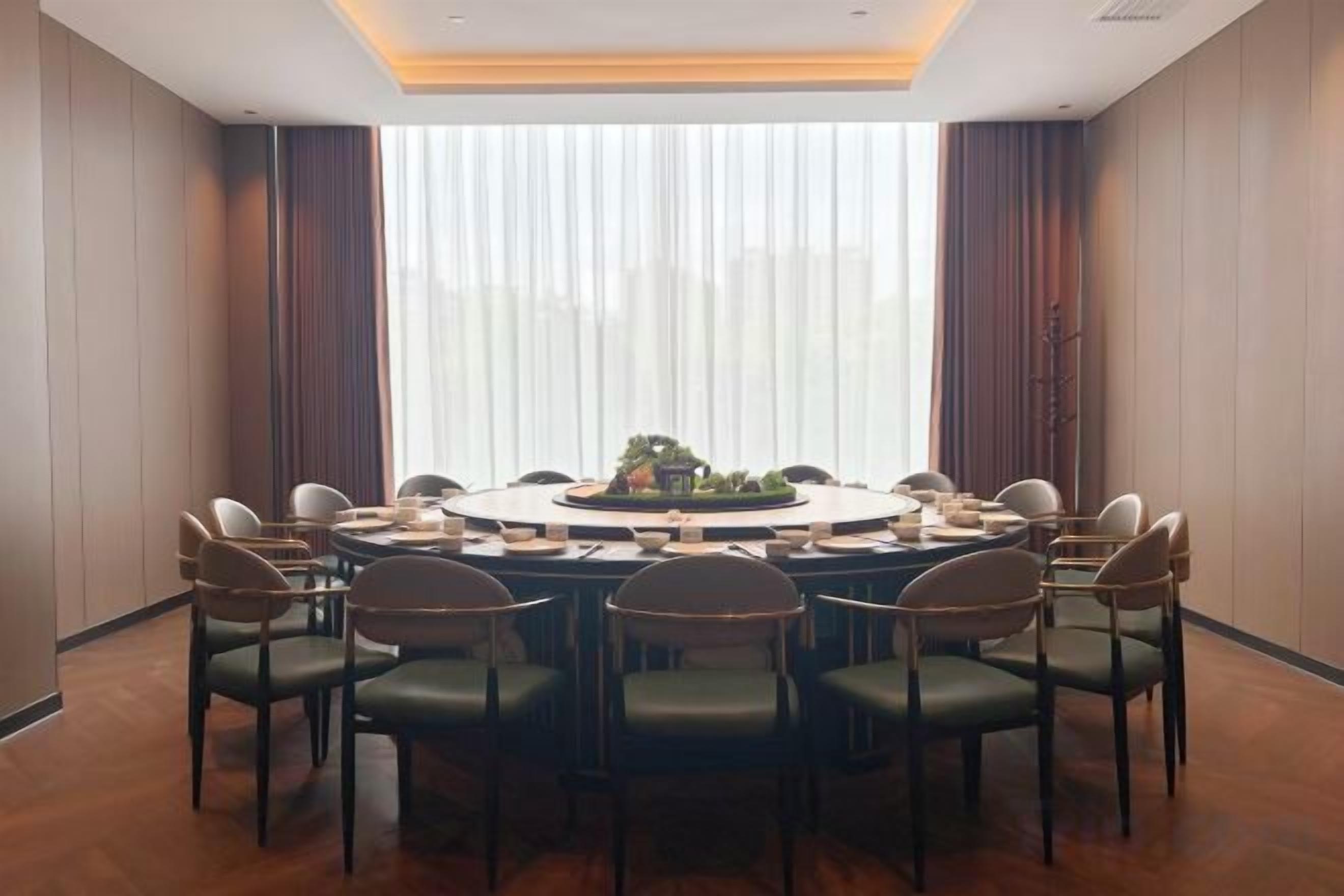 Una sala de conferències amb una taula rodona, cadires i un finestral gran amb cortines.