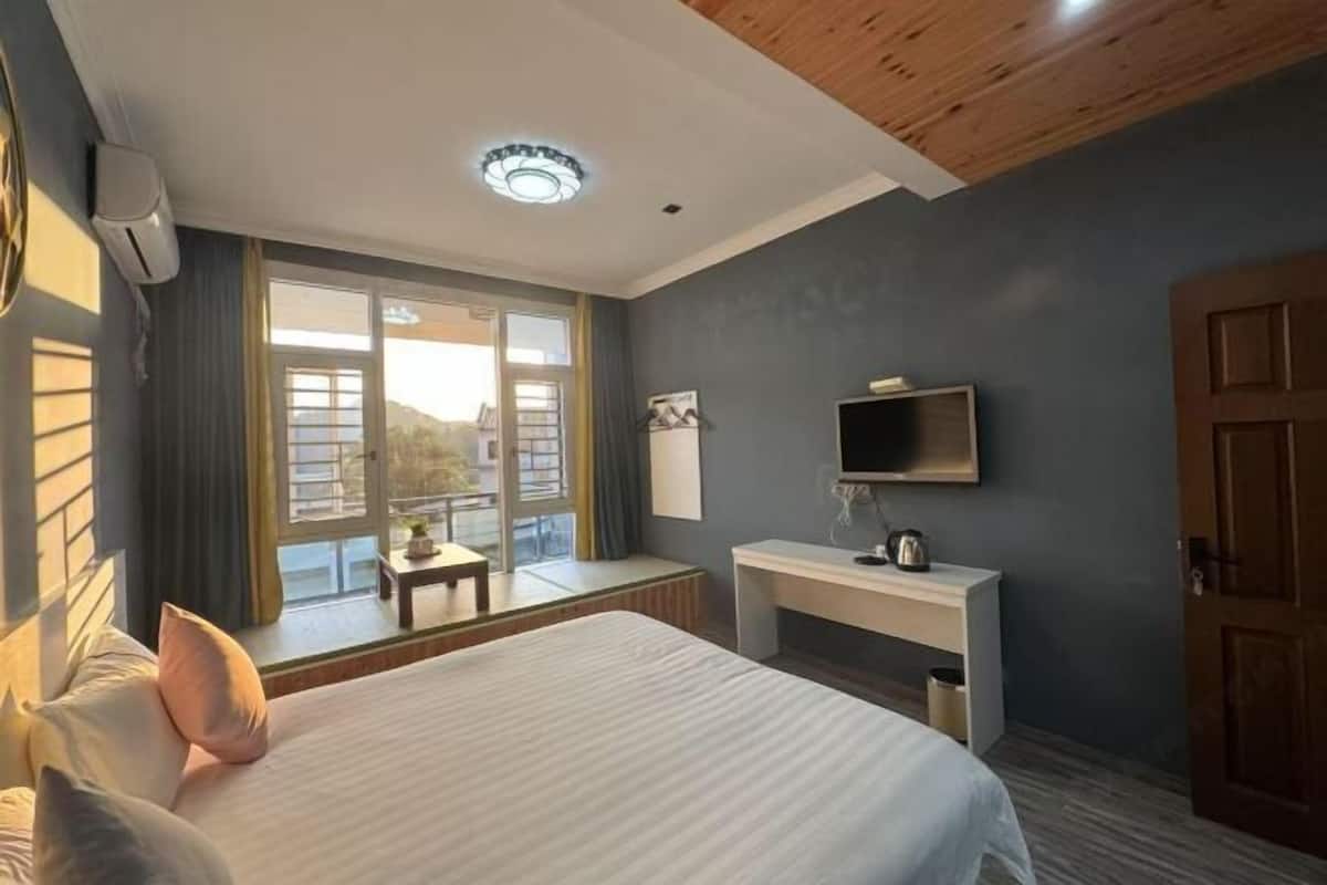 A bedroom with a bed, a TV, a desk, and a window with a view.