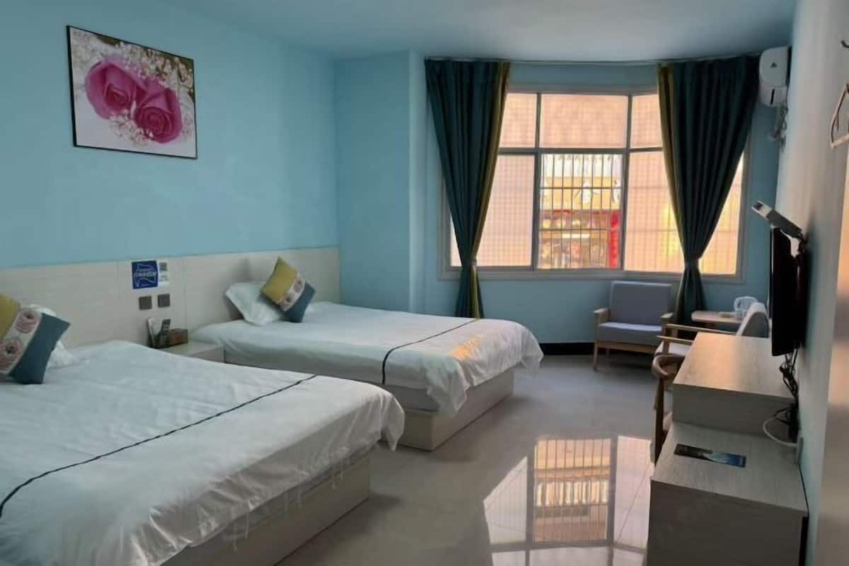 A hotel room with two beds, a desk, a chair, a window with curtains, and a wall-mounted TV.