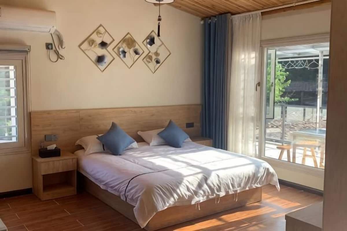 A bedroom with a wooden headboard, a large bed with white bedding, two bedside tables, and a view of the outdoors through a glass door.