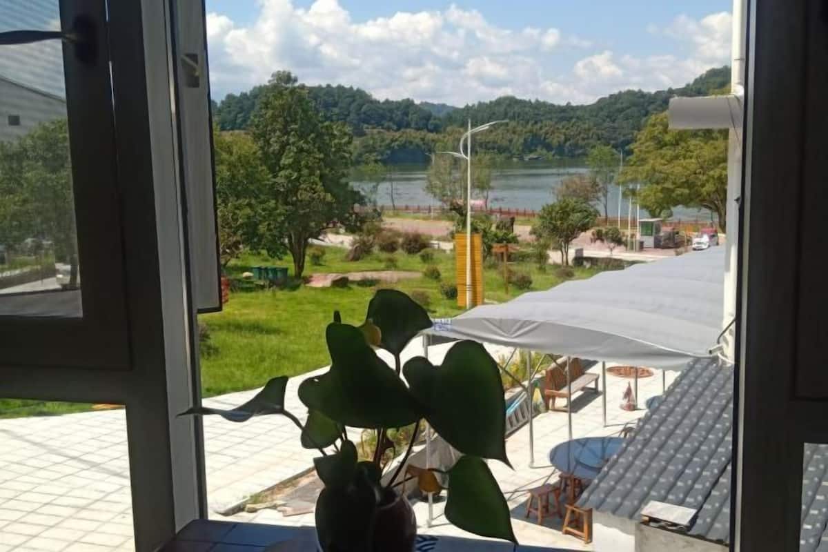 A view from a window overlooking a lake, a grassy area, and a building with a white awning.