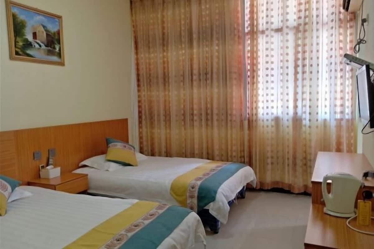 A hotel room with two beds, a wooden headboard, a desk with a kettle, and a painting on the wall.