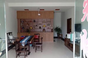 A dining area with a table and chairs, wooden cabinets with decorative items, and a television on a stand. - Taining Dajinhu Xiuzhen Homestay (Taining)