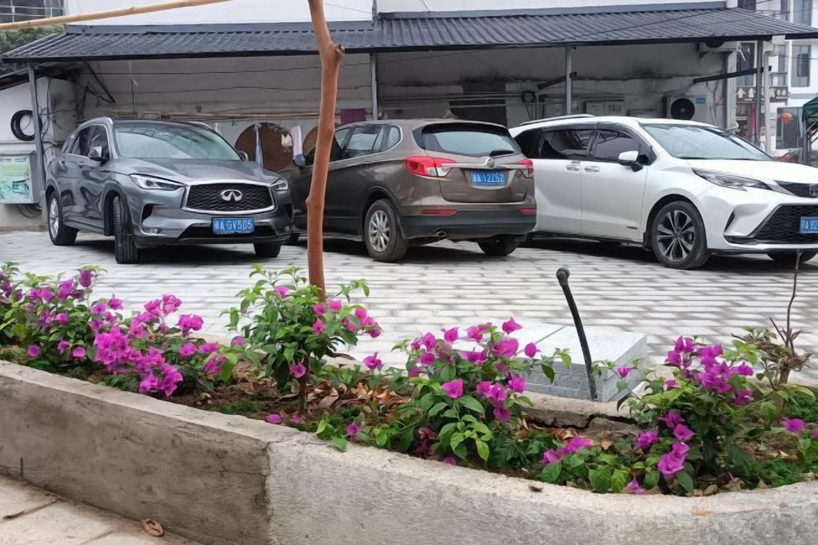 Een parkeerplaats met drie auto's, een overdekte constructie en een bloembed met roze bloemen.