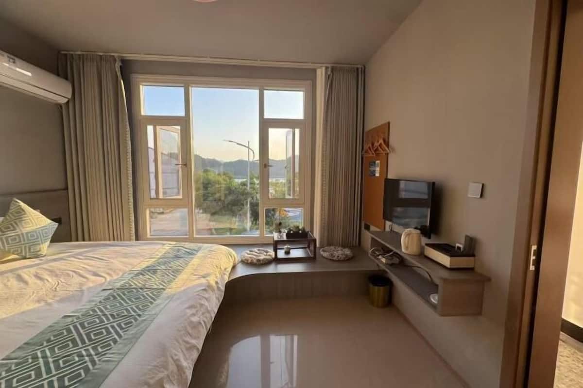 A hotel room with a bed, a TV, a small table, and a window with a view of the outdoors.