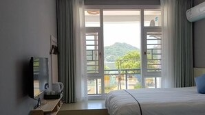 A hotel room with a bed, a TV, a coffee maker, and a balcony with a view of greenery.