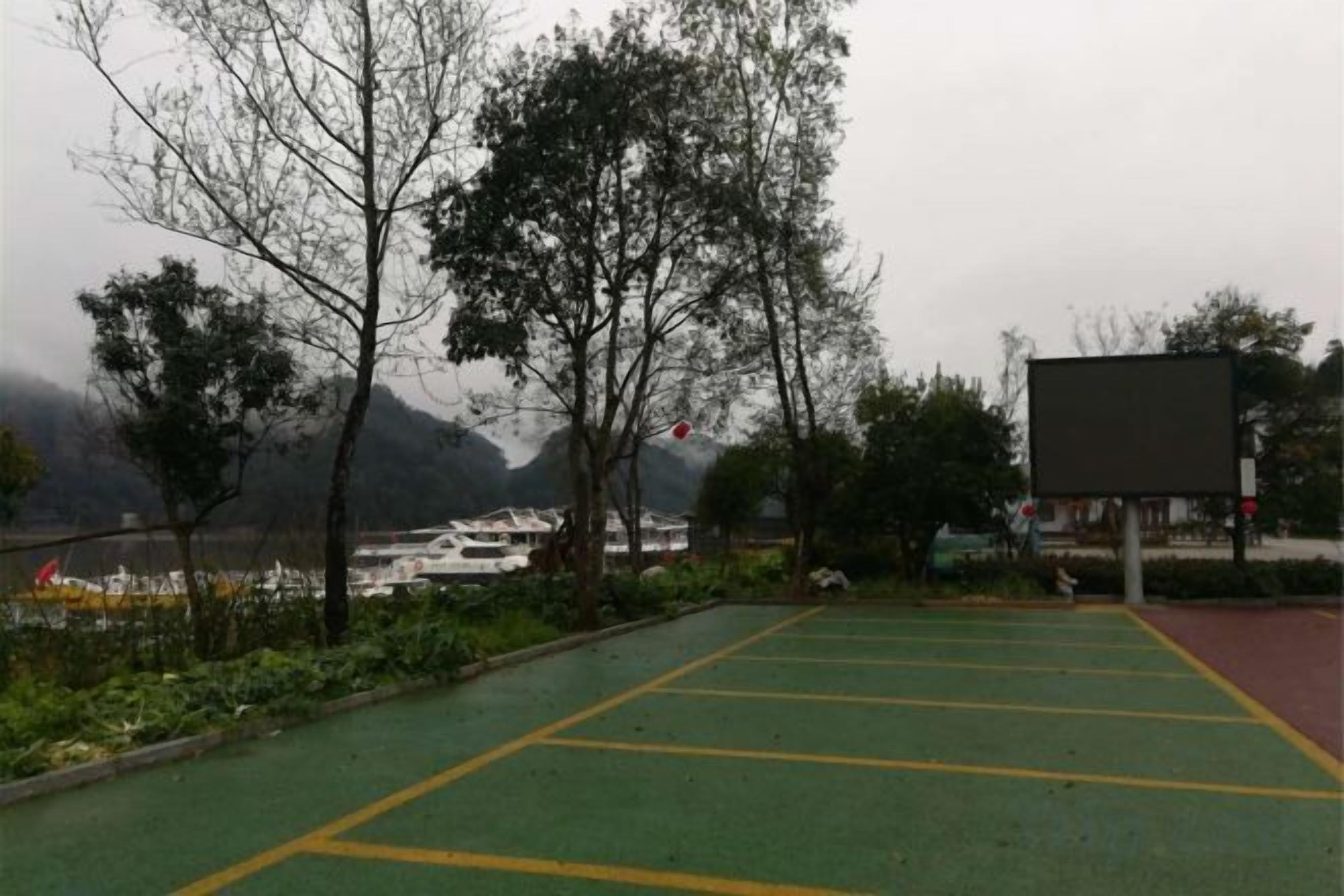 Un área de estacionamiento con marcas verdes y amarillas, rodeada de árboles y vistas a montañas.