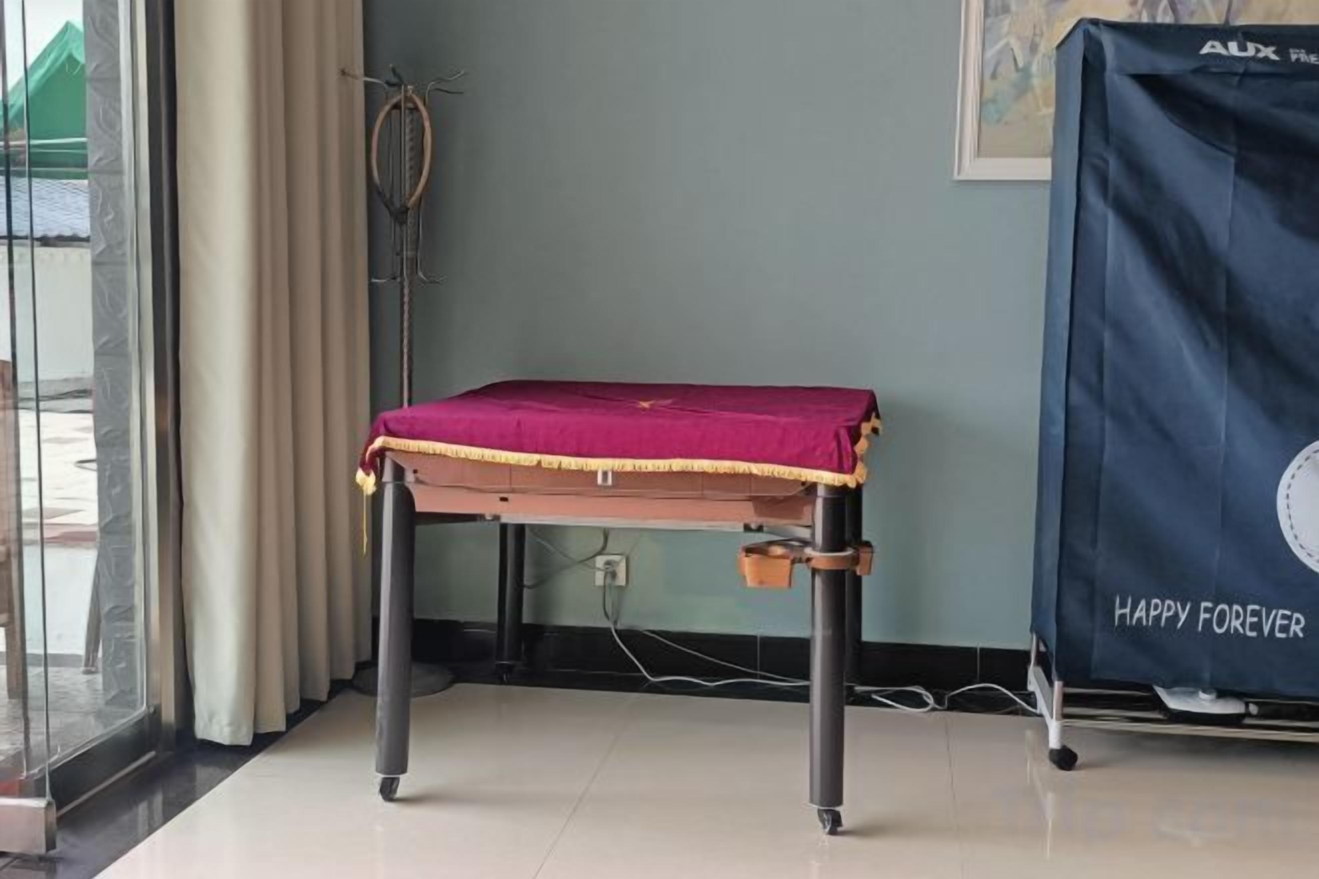 A room with a table covered by a red cloth, a curtain, a wall-mounted speaker, and a framed picture.