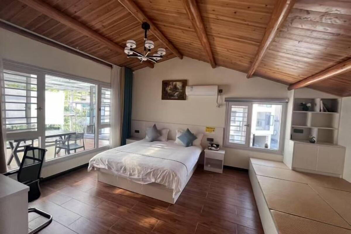 A bedroom with a wooden ceiling, a bed with pillows, a nightstand, a window, and a chair.