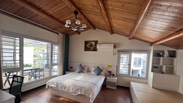 A bedroom with a wooden ceiling, a bed with pillows, a nightstand, a window, and a chair.