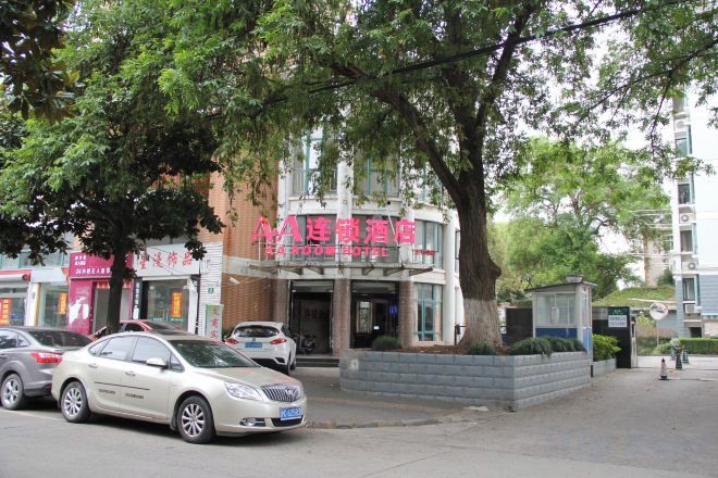 A hotel with a red sign, parked cars, and a tree in front.