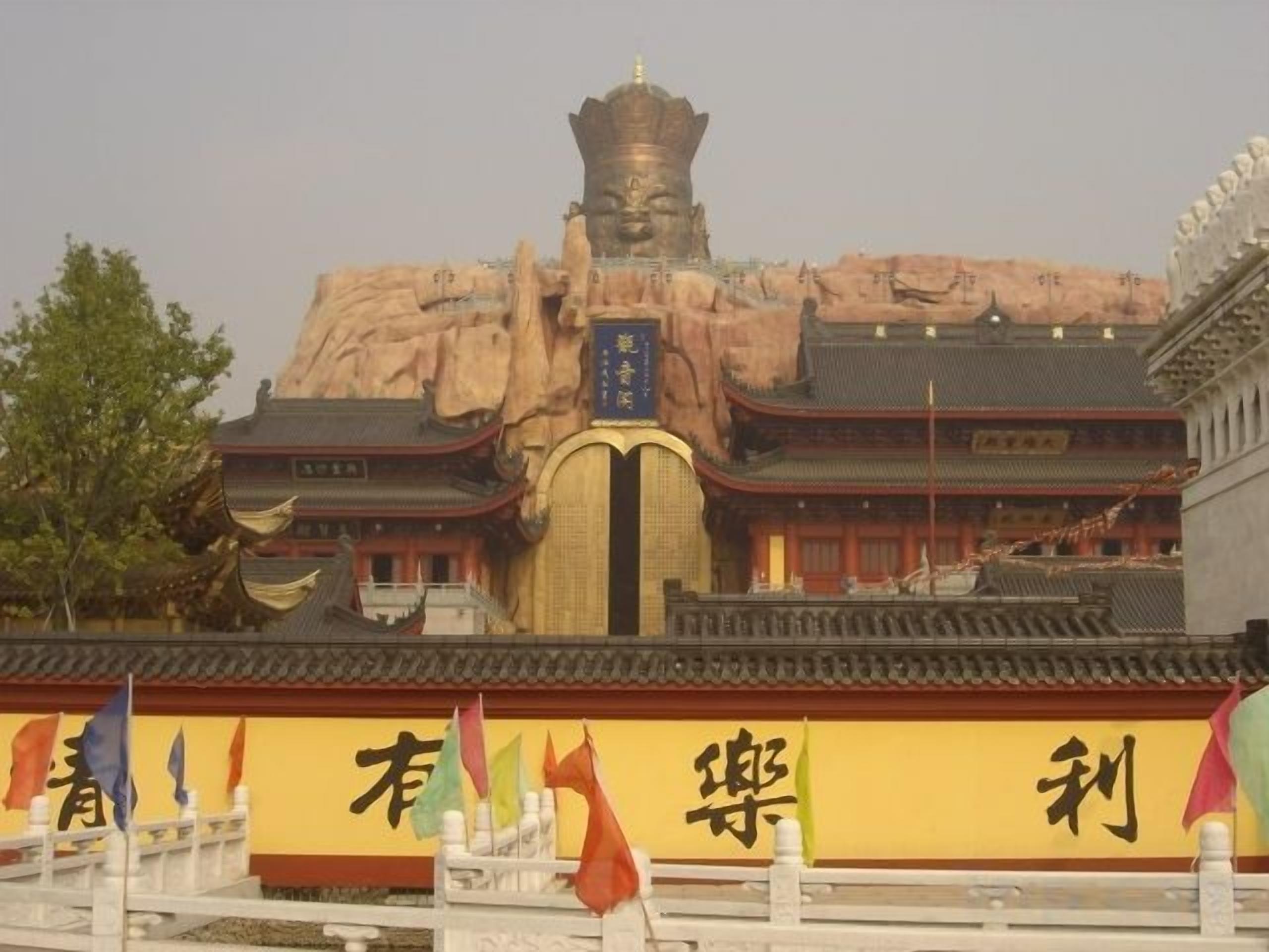 A traditional building with a prominent rock formation in the background, a tiled roof, and a banner with Chinese characters.