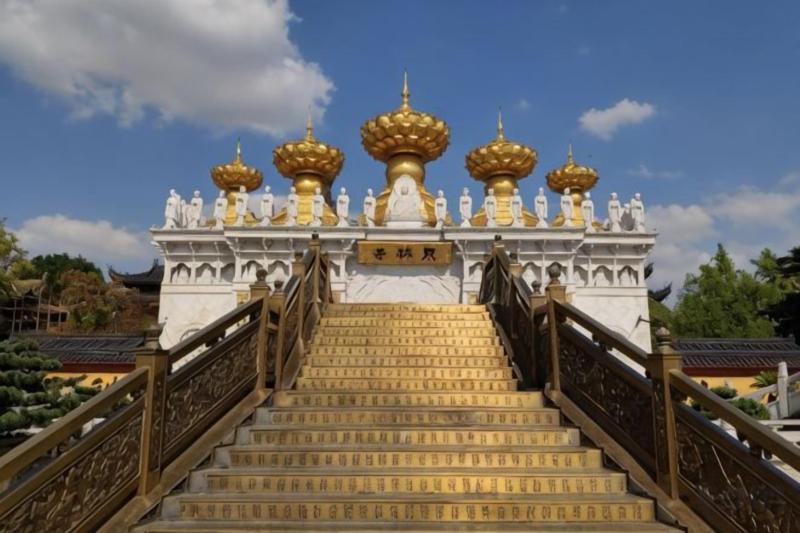 A temple entrance with a staircase leading up to a structure with golden domes.