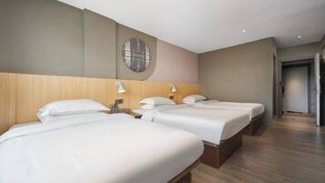 A hotel room with three beds, wooden headboard, wall-mounted lamps, and a circular wall decoration.