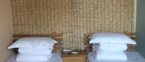 Two single beds with wooden headboards, a woven wall, and a small table between them.