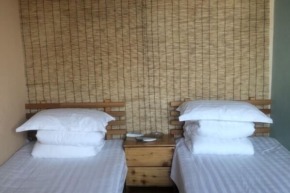 Zwei Einzelbetten mit Holz-Kopfteilen, eine gewebte Wand und ein kleiner Tisch dazwischen.