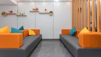 A reception area with two grey sofas, orange cushions, and wooden shelving with decorative items.