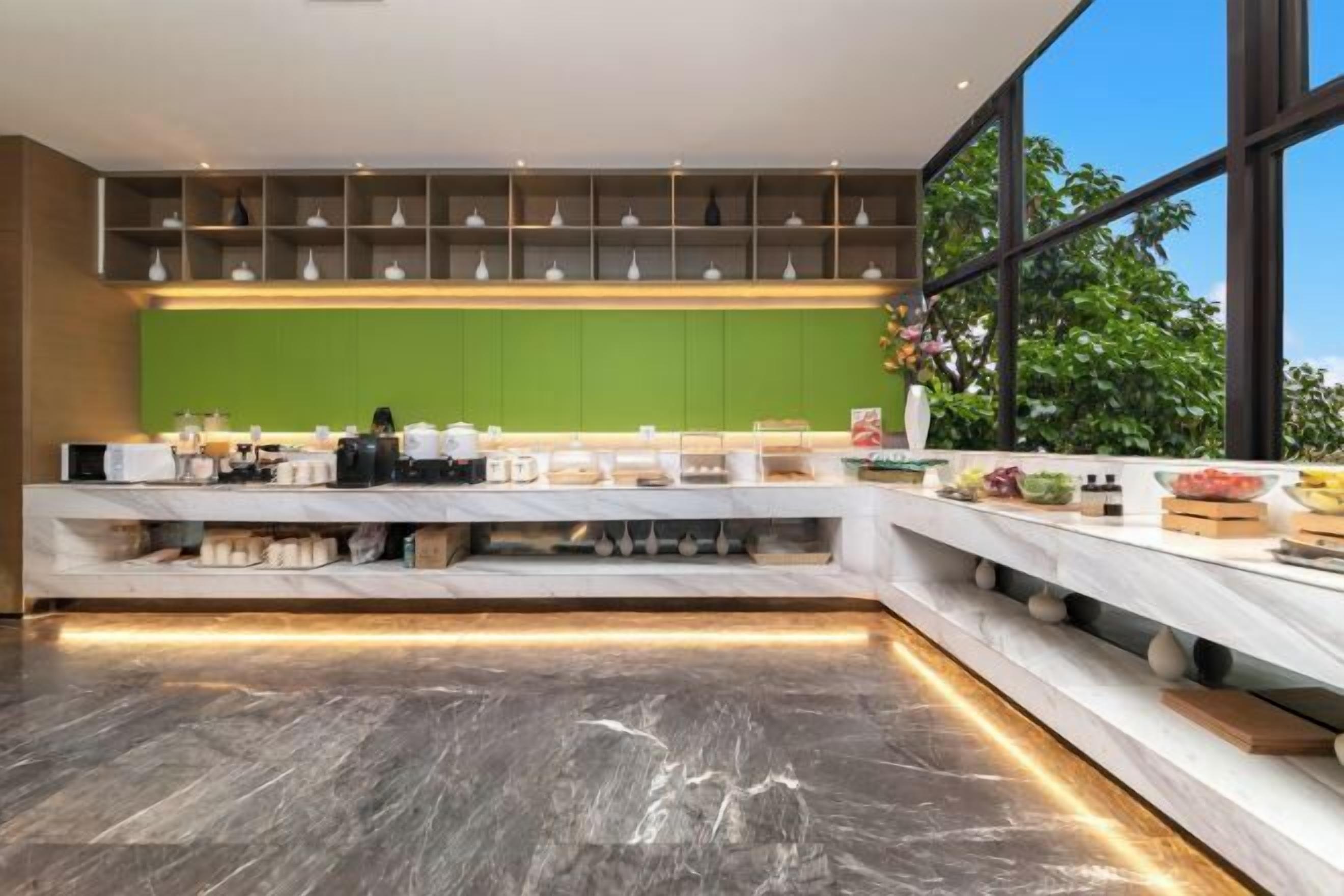 Cocina moderna con pared verde de acento, encimeras de mármol y una ventana grande que ofrece vistas a zonas verdes.