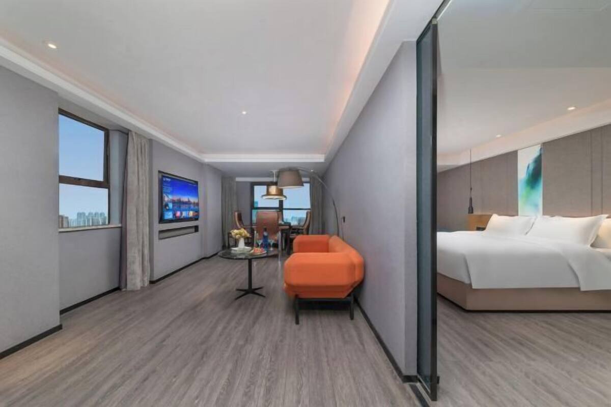 A modern hotel room with a bed, a TV, a seating area, and a view of the city.