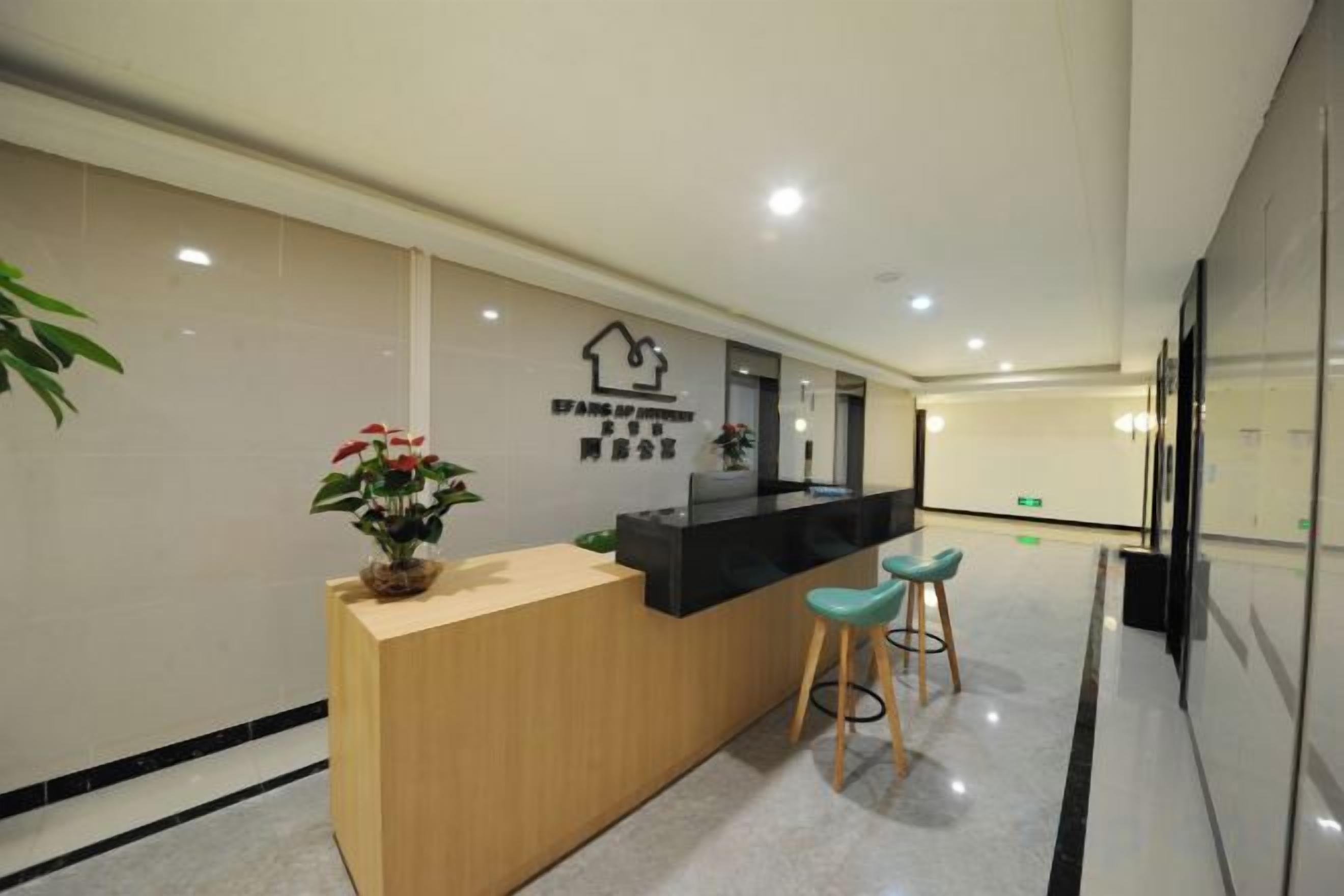 A reception desk with a wooden counter, two bar stools, a potted plant, and a wall-mounted sign.