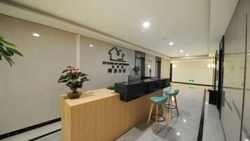 A reception desk with a wooden counter, two bar stools, a potted plant, and a wall-mounted sign.