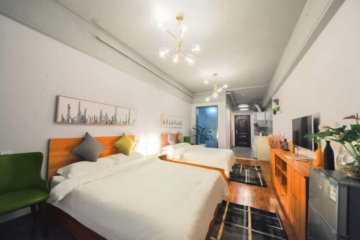 Una habitación de hotel con dos camas, una silla verde, un armario de madera y un televisor.
